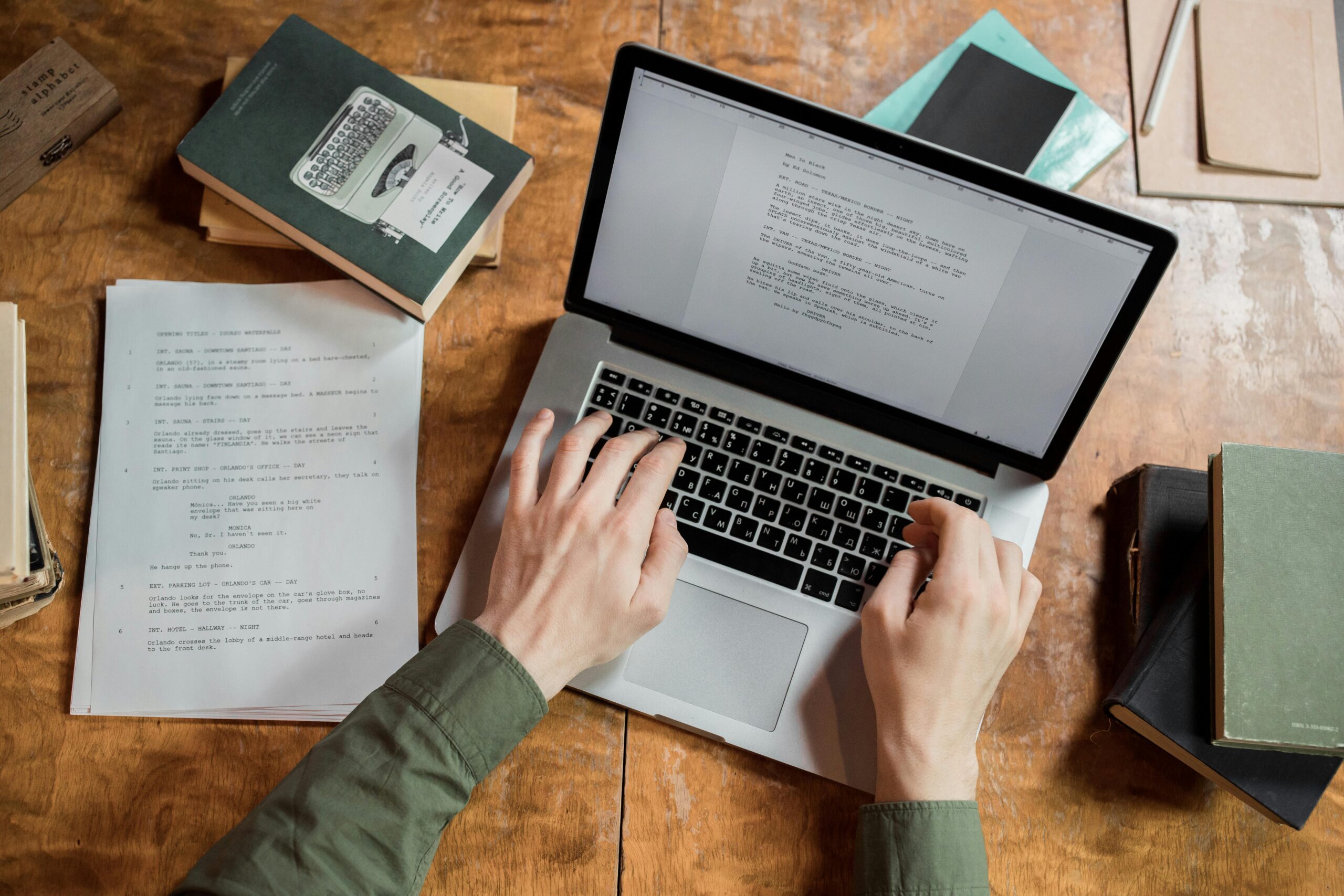 A man typing on a computer with books and papers stacked next to him